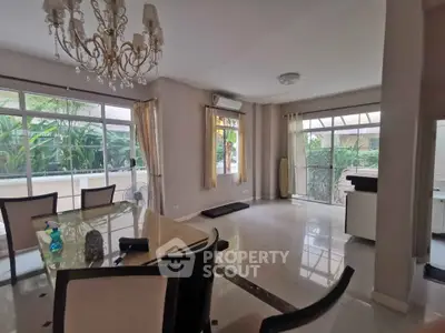 Spacious dining area with elegant chandelier and large windows overlooking lush greenery.
