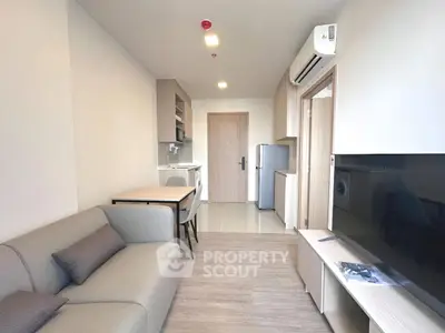 Modern living room with open kitchen, featuring sleek furniture and appliances.
