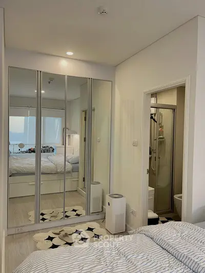 Modern bedroom with mirrored closet doors and ensuite bathroom, featuring stylish decor and natural light.