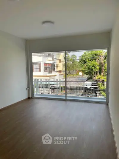 Spacious room with large window offering a view of the street and greenery, perfect for natural light.