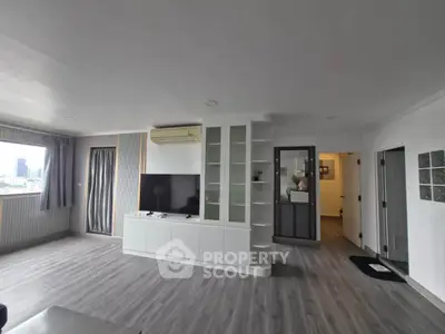 Spacious modern living room with sleek flooring and large TV, perfect for relaxation.