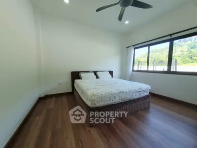 Spacious bedroom with large window and scenic view, featuring a comfortable bed and modern ceiling fan.