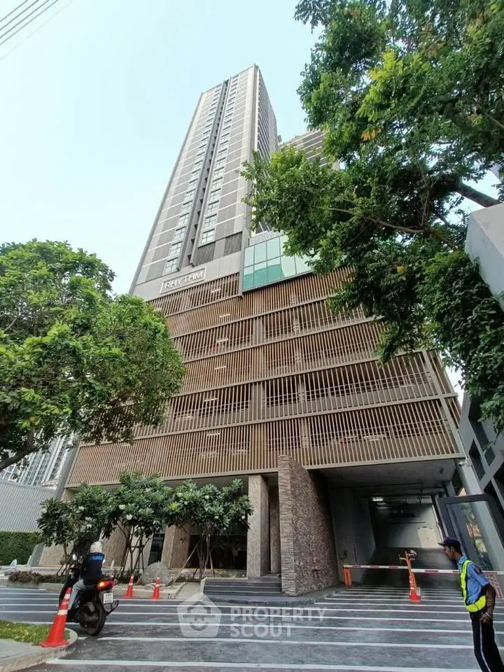 Modern high-rise building with sleek design and lush greenery at entrance.