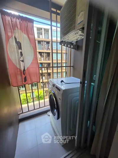 Compact balcony with washing machine and curtain, overlooking modern apartment complex.
