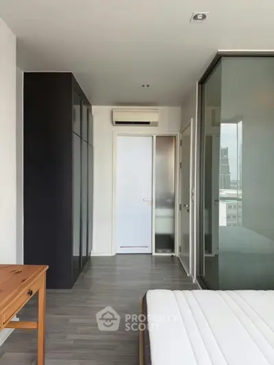 Modern bedroom with sleek design and city view, featuring glass wardrobe and air conditioning.