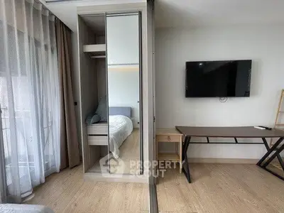 Modern bedroom with mirrored wardrobe, wall-mounted TV, and sleek desk in a stylish apartment.