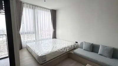 Modern bedroom with large window and city view, featuring a cozy sofa and minimalist decor.