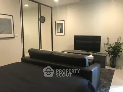 Modern bedroom with sleek black sofa and wall-mounted TV, minimalist decor and framed art.
