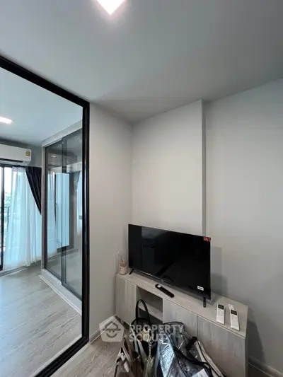 Modern living room with sleek TV setup and glass sliding doors leading to a bright balcony.
