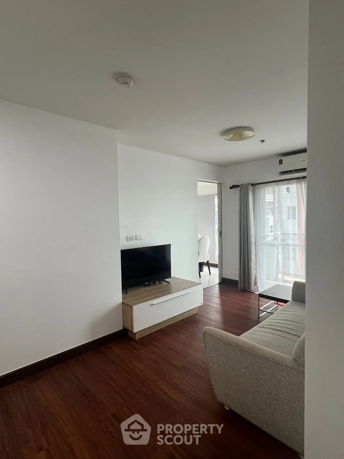 Modern living room with sleek wooden flooring and natural light from large windows.
