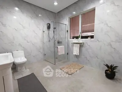 Spacious modern bathroom with elegant marble walls and glass shower enclosure.