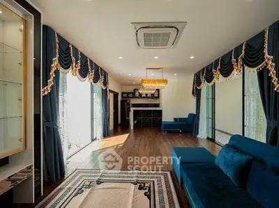 Luxurious living room with elegant drapes and plush blue sofas, featuring a stylish chandelier and wooden flooring.