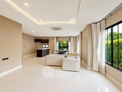 Spacious modern living room with open kitchen and large windows overlooking lush greenery.