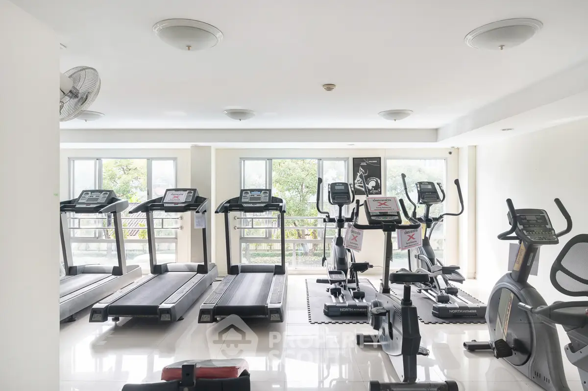Spacious gym with modern exercise equipment and large windows for natural light.