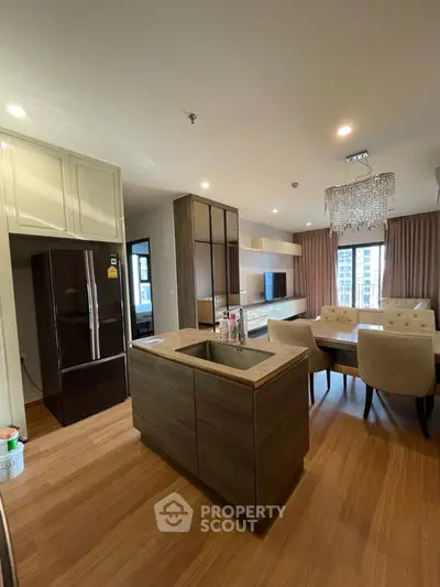 Modern open-plan kitchen and dining area with elegant chandelier and large windows.