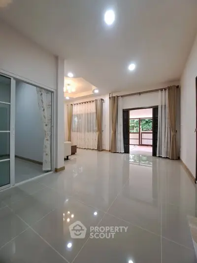 Spacious living room with glossy tiled floors and large windows leading to a balcony.