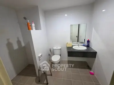 Spacious bathroom with modern fixtures and tiled walls, featuring a large mirror and ample lighting.