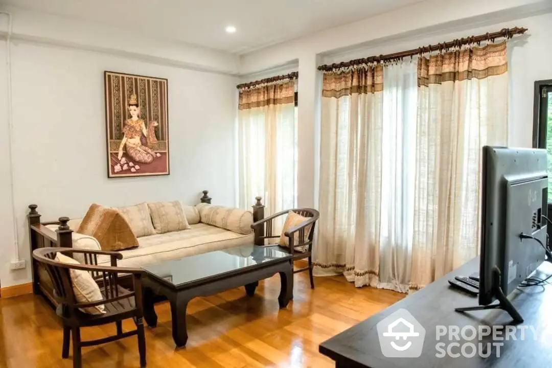 Elegant living room with polished hardwood floors, traditional furniture, and natural light filtering through sheer curtains.