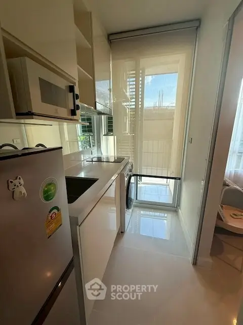 Modern kitchen with sleek appliances and natural light, featuring a washing machine and balcony access.