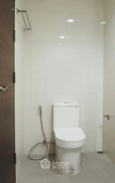 Modern bathroom with sleek white toilet and bidet spray, featuring minimalist design and neutral tones.
