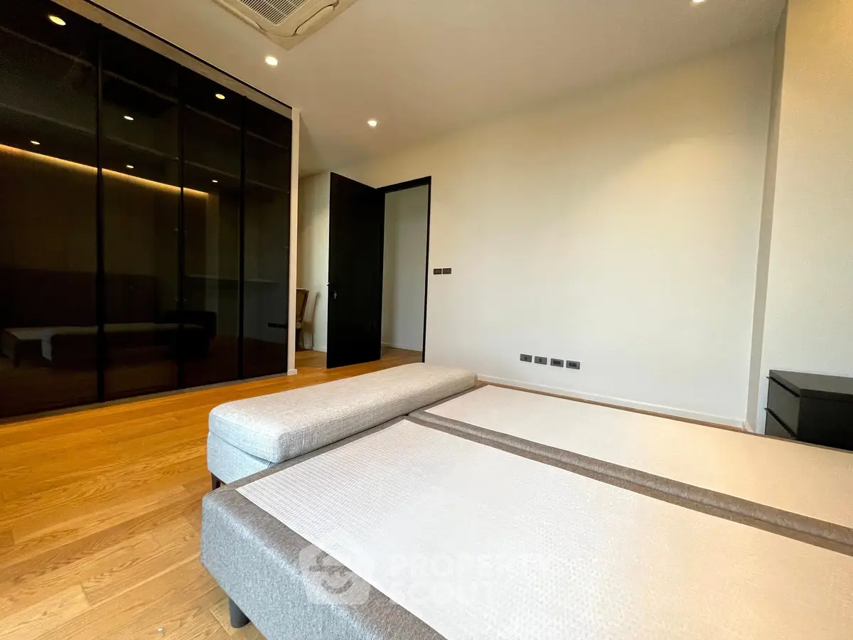 Spacious modern bedroom with sleek wooden flooring and stylish black wardrobe.