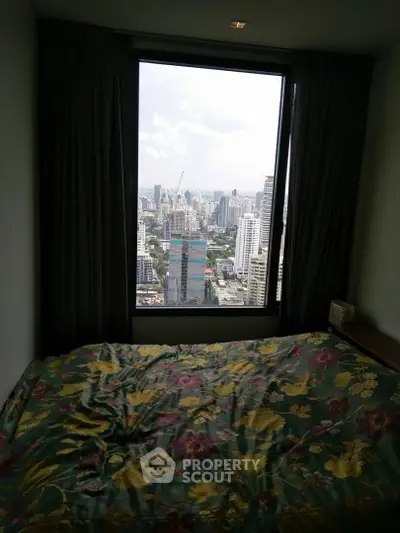High-rise bedroom with stunning city view through large window, featuring cozy floral bedding.