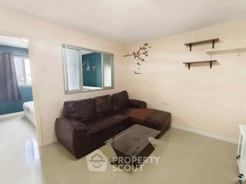 Cozy living room with brown leather sofa and glass coffee table, adjacent to a bright bedroom.