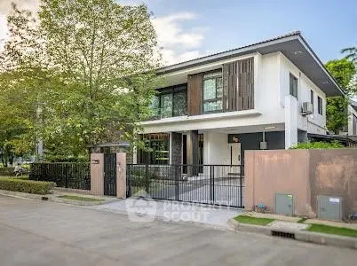Modern two-story house with gated entrance and lush greenery