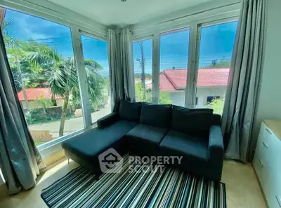 Bright living room with large windows and cozy sofa, offering a serene view of lush greenery.