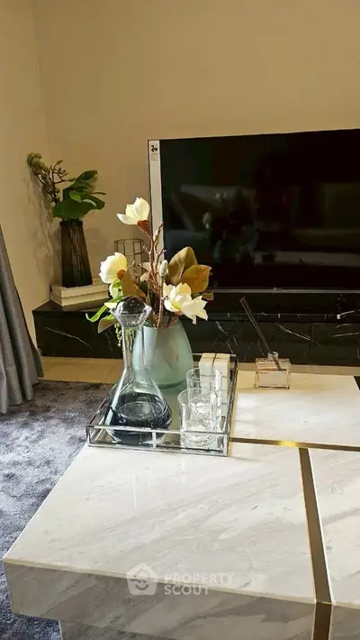 Elegant living room with modern decor and large TV, featuring a stylish marble coffee table and decorative plants.