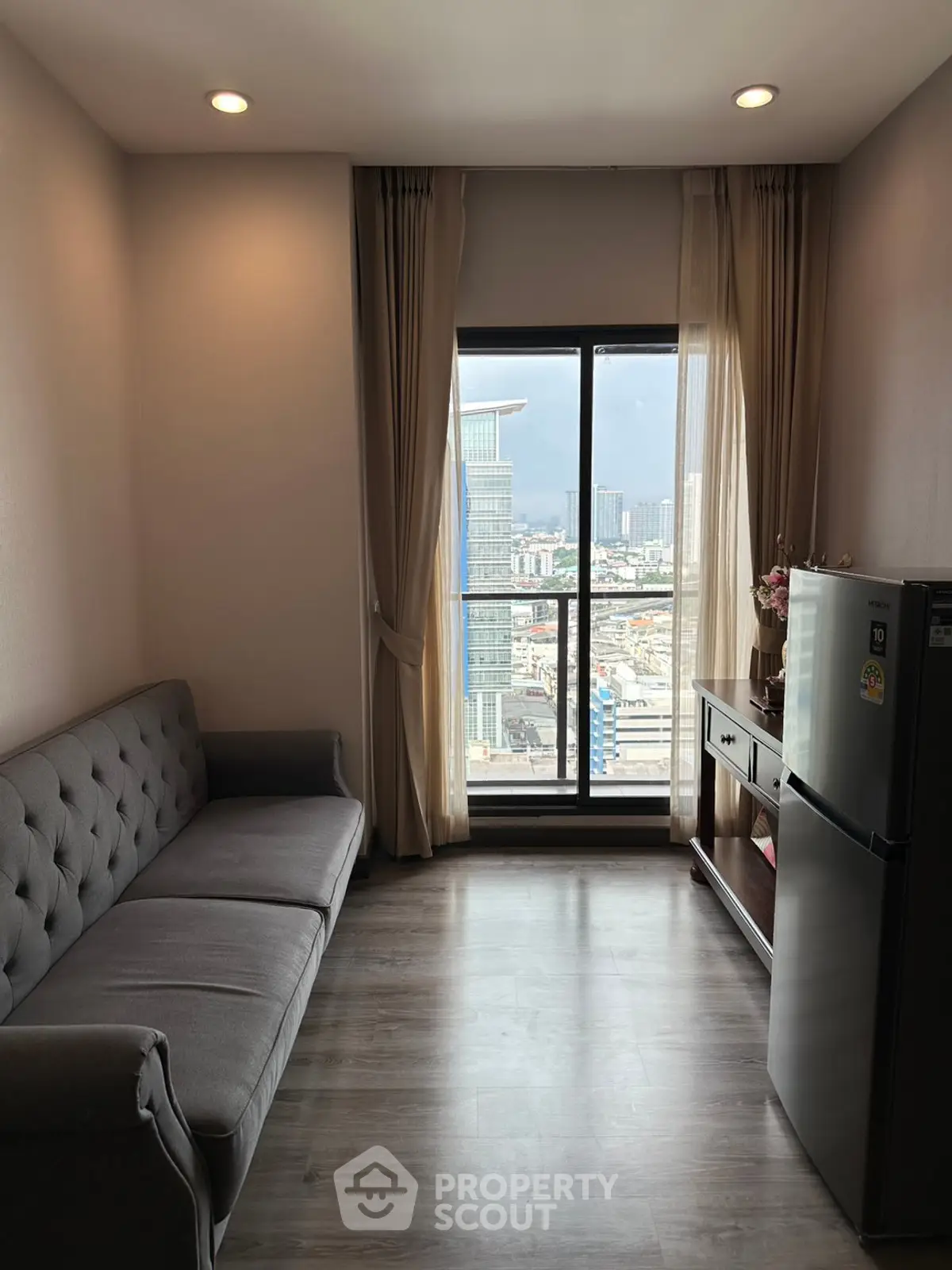 Modern living room with city view, featuring a sleek sofa and compact fridge.