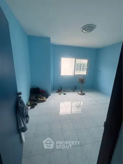 Spacious blue-walled room with tiled flooring and window view, ideal for customization.