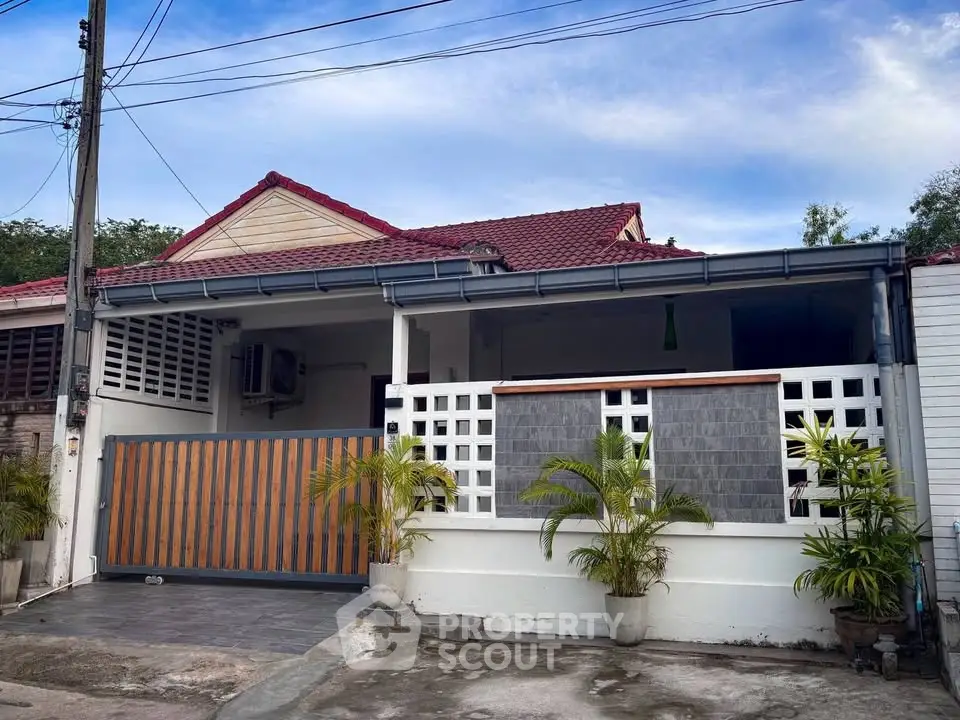 Charming single-story home with red roof and gated entrance, featuring a cozy front patio and lush greenery.