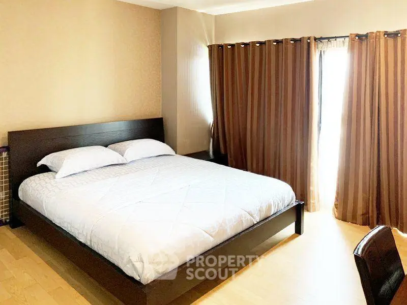 Spacious bedroom with large bed and elegant curtains in modern apartment.
