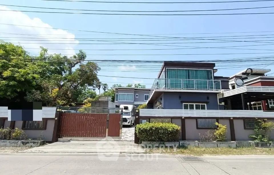 Modern two-story house with spacious balcony and gated entrance in a suburban neighborhood.