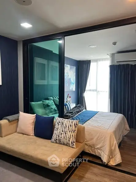 Modern bedroom with glass partition and cozy seating area, featuring stylish decor and natural light.
