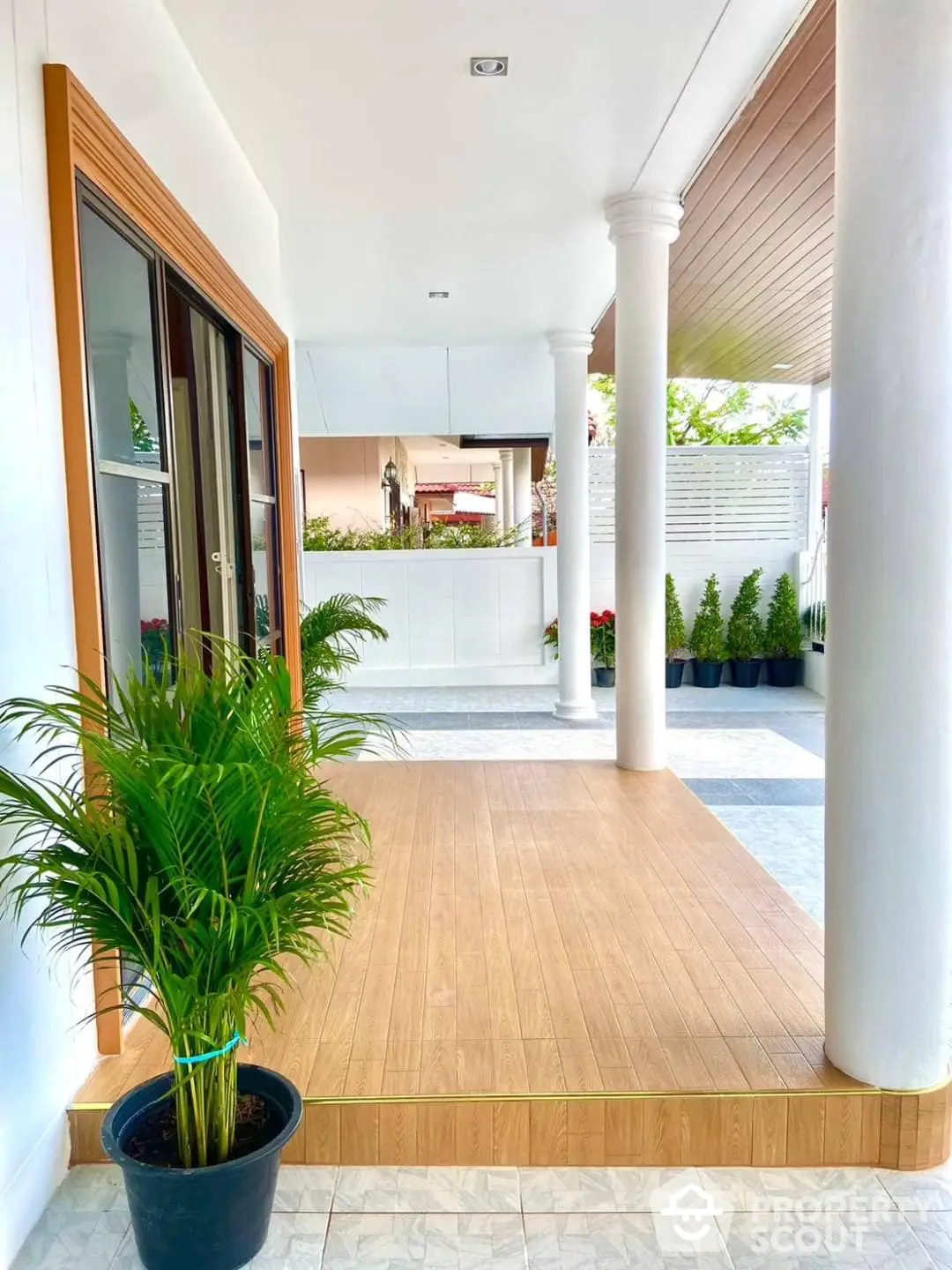 Spacious and elegant covered porch area with polished wooden flooring, classic white columns, and lush potted plants enhancing the welcoming ambiance of a luxurious home.