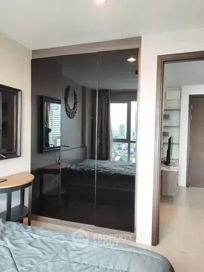 Modern bedroom with sleek mirrored wardrobe and city view window.