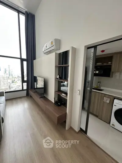Modern living room with high ceiling and city view, adjacent to sleek kitchen area.