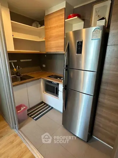 Modern compact kitchen with stainless steel fridge and wooden cabinets in a cozy apartment.