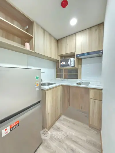Modern compact kitchen with wooden cabinets and stainless steel appliances in a cozy apartment.