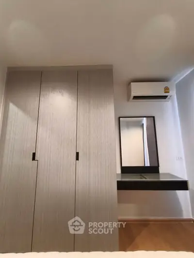 Modern bedroom with sleek wardrobe and air conditioning unit, featuring a minimalist design and functional layout.