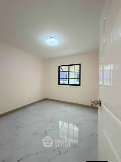 Spacious empty room with marble flooring and bright window, perfect for customization.