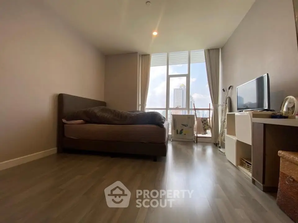 Spacious bedroom with city view and modern furnishings in high-rise apartment.