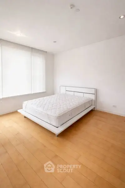 Spacious minimalist bedroom with natural light and wooden flooring.