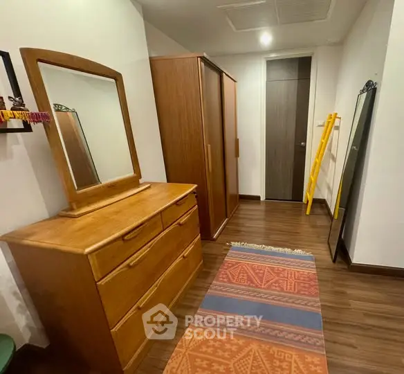 Spacious bedroom with wooden furniture and colorful rug, offering ample storage space.