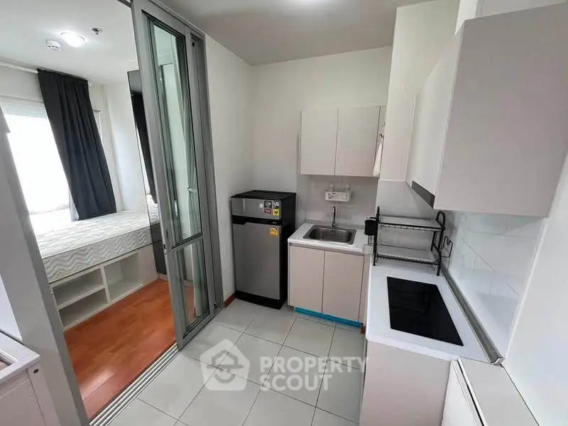 Modern compact kitchen with sleek appliances and adjacent cozy bedroom in a stylish apartment.