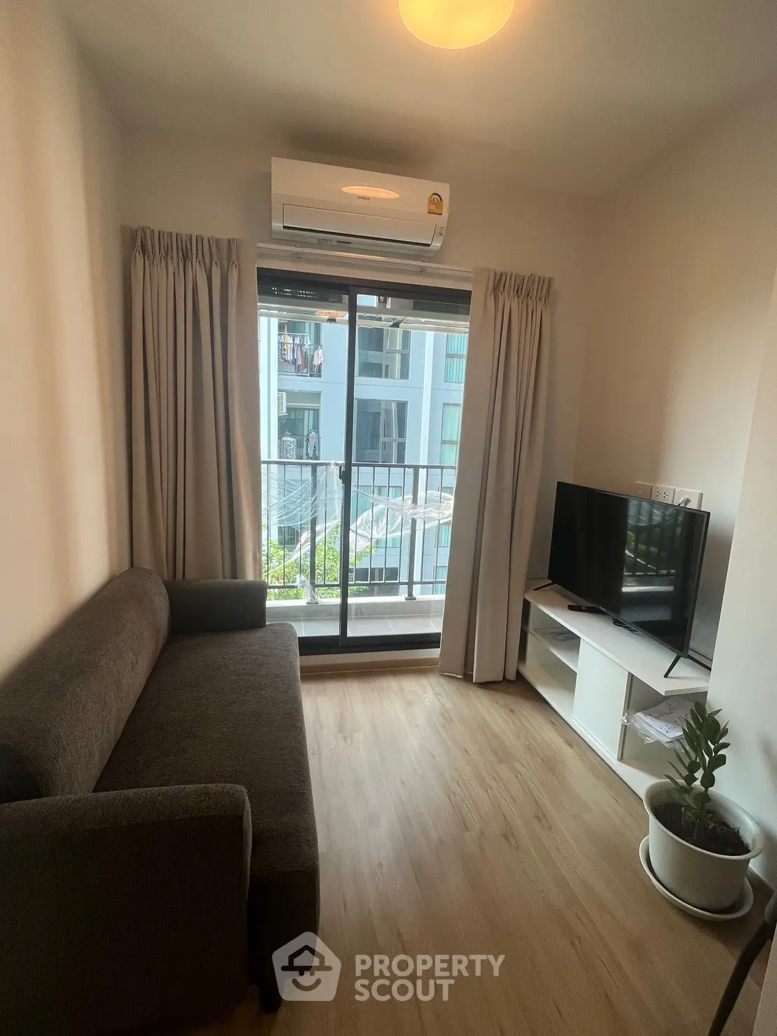 Cozy living room with balcony view, featuring a sofa, TV, and air conditioning.