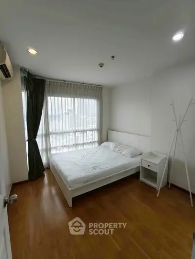 Spacious bedroom with large window and wooden flooring in modern apartment.