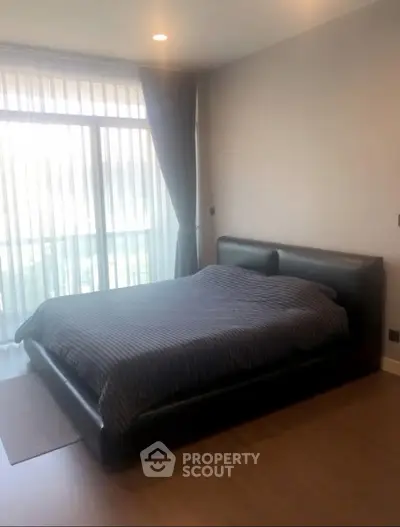 Spacious bedroom with large window and modern furnishings in a stylish apartment.